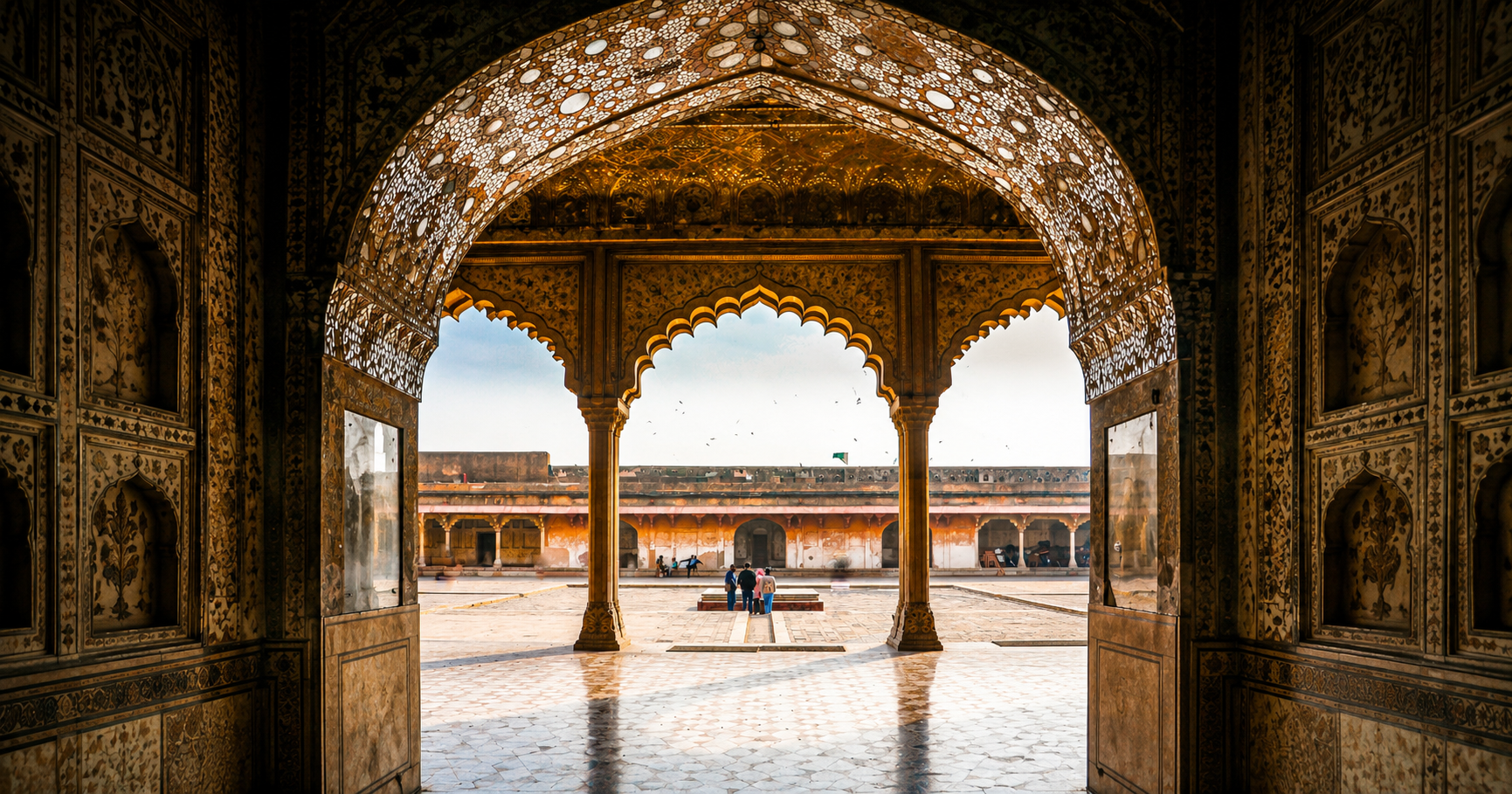 An ornate Mughal archway framing a sunlit courtyard, with gold and floral fresco work covering the ceiling and walls.